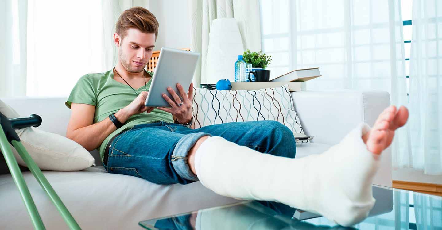 Mann mit Gips auf der Couch benutzt ein Tablet.